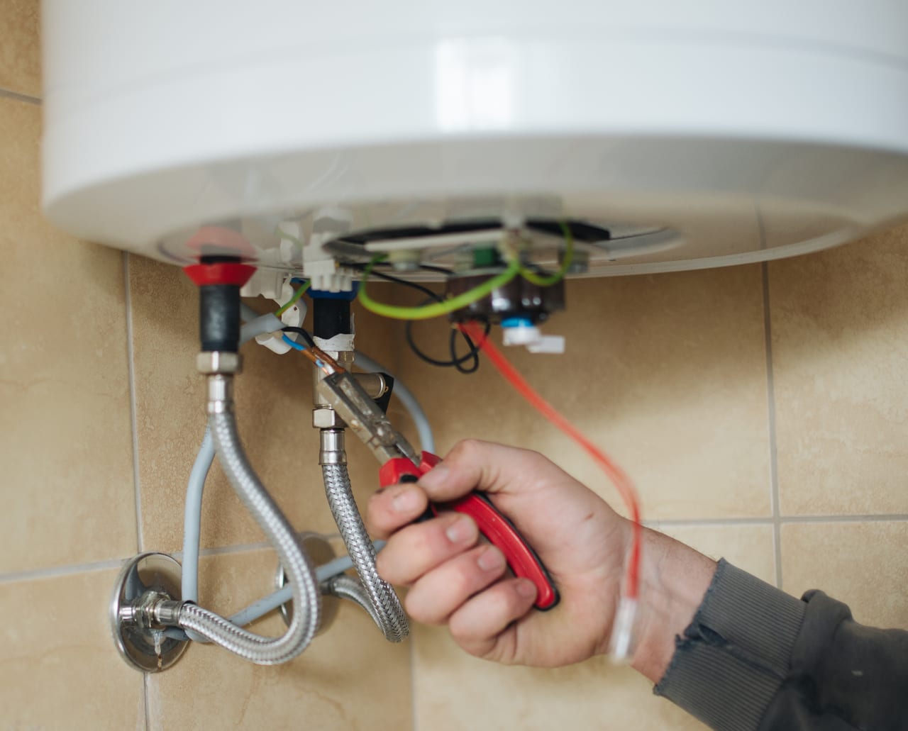 Hands using pliers at the open service panel of a compact water heater