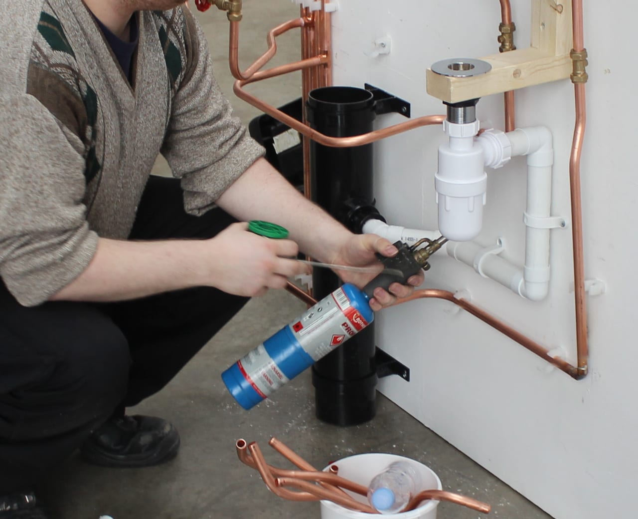 Hands, a tool and pipe connections in a plumbing practice assembly